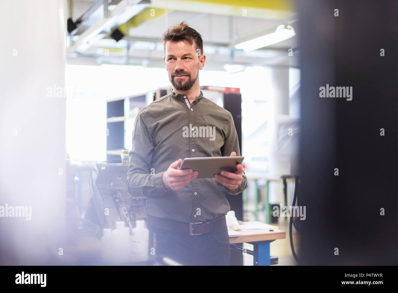 Smiling man standing en usine avec tablet looking sideways Banque D'Images