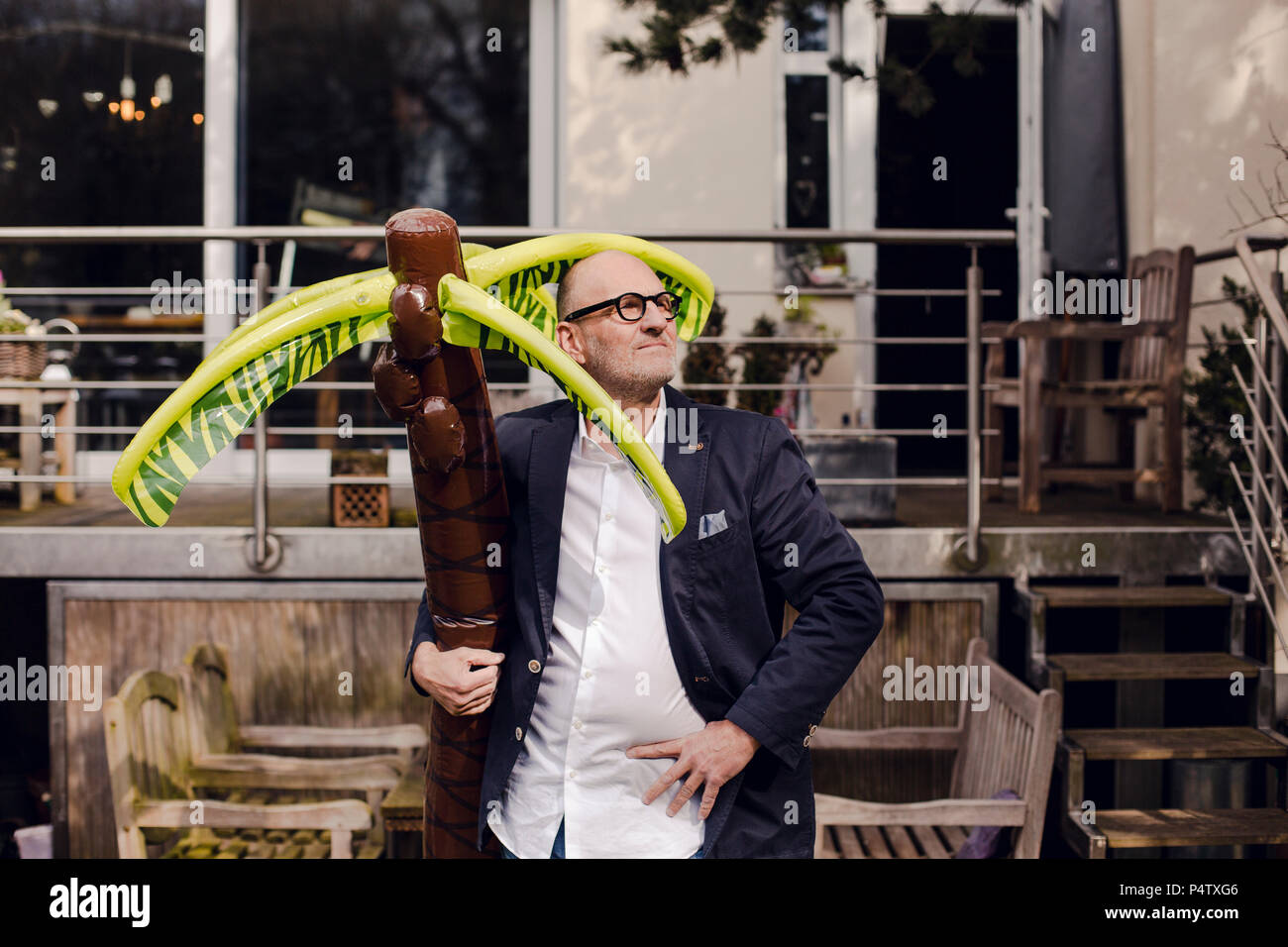 Senior businessman debout dans son jardin, tenant une palme en caoutchouc, rêvant de vacances Banque D'Images