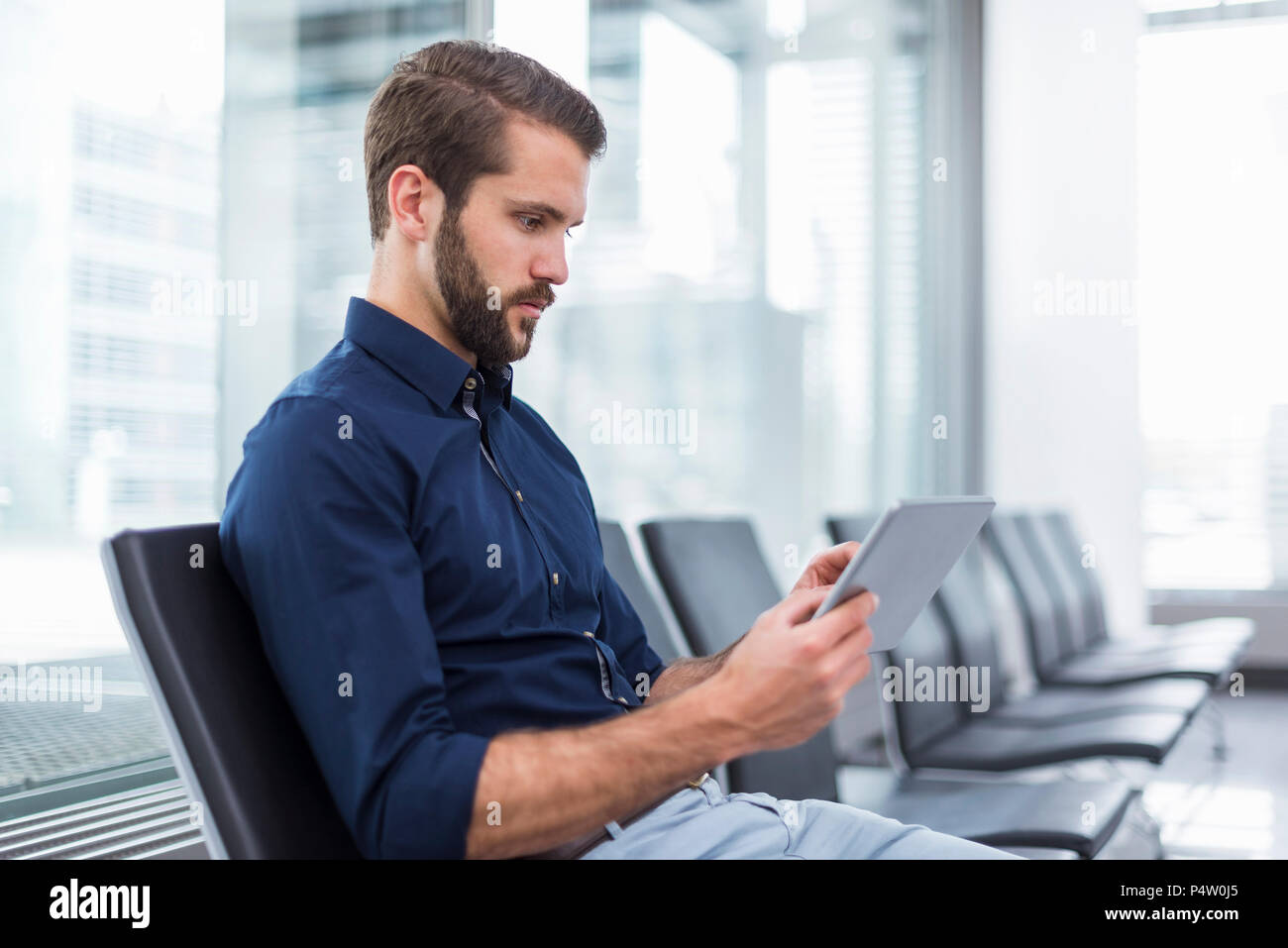 Young businessman sitting in waiting area en utilisant tablet Banque D'Images