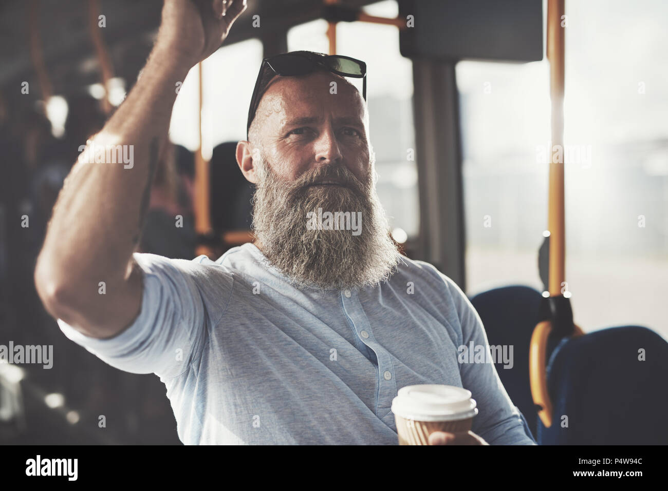 Homme mature avec une longue barbe et de boire une tasse de café à emporter en étant debout sur un bus pendant son trajet du matin Banque D'Images