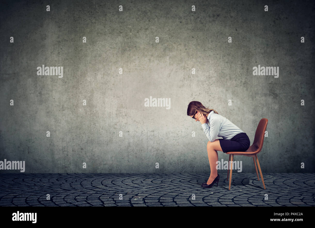 Femme d'affaires déprimé contrarié par la mauvaise chance assis sur une chaise contre le seul mur gris Banque D'Images