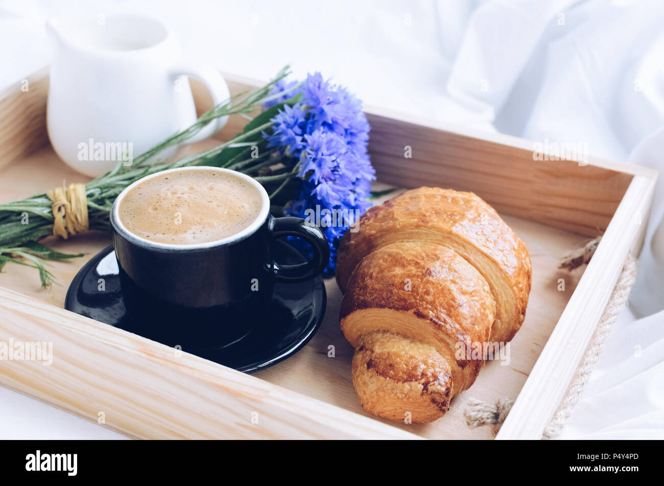 De l'été romantique petit-déjeuner au lit, plateau avec croissant frais, tasse de café espresso avec lait et bouquet de bleuets bleu. Bon matin concept. E Banque D'Images