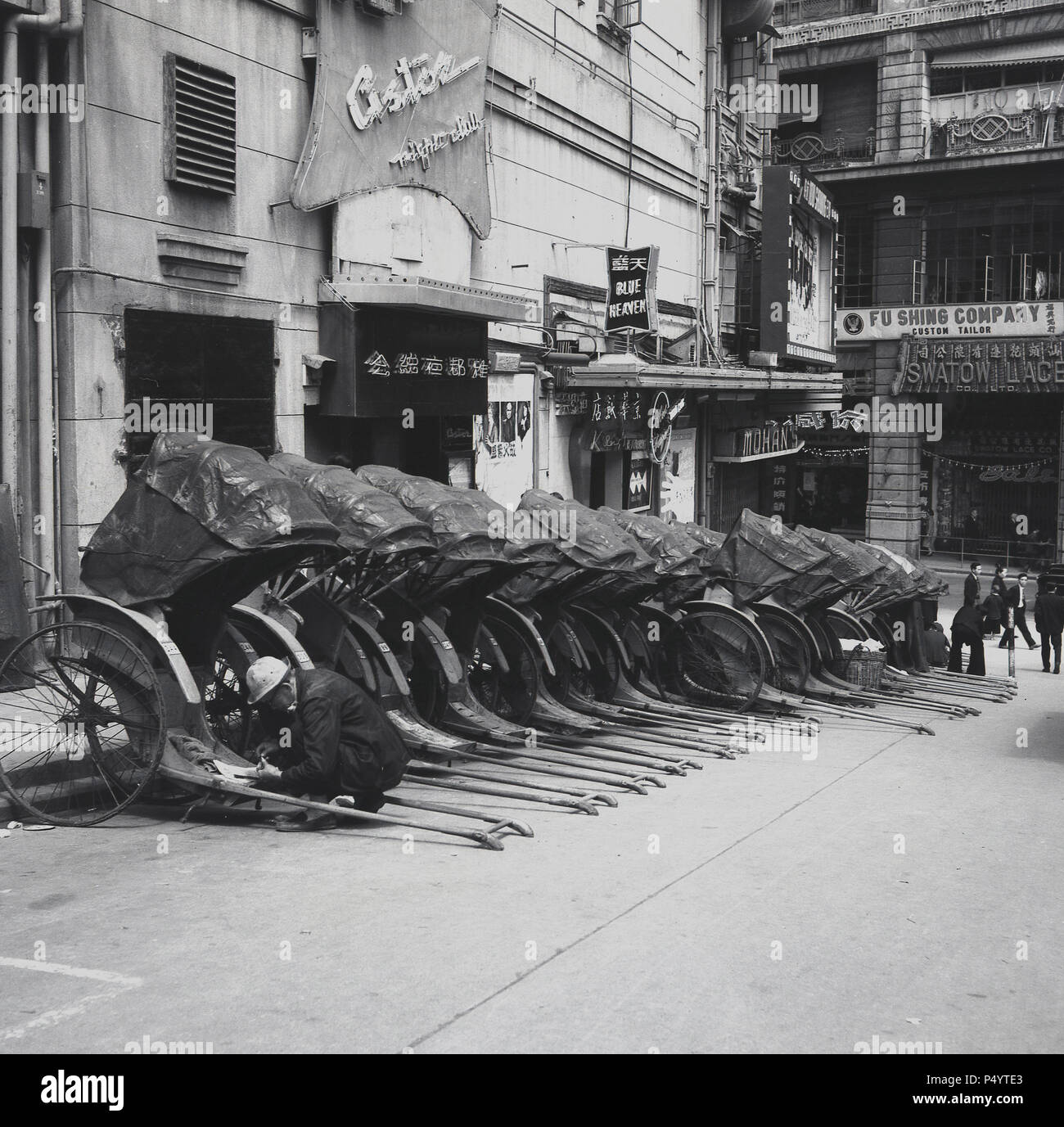 Années 1950, historique, garée dans une petite rue de la vieille ville de Hong Kong, une ligne de rickshaws avec des capots.Ces chariots de transport de passagers à deux roues motorisés par un homme, où une personne tire une autre personne, étaient une forme de transport populaire dans de nombreuses villes asiatiques.Le mot rickshaw est originaire du mot japonais pour « véhicule à moteur humain ».Le pousse-pousse original est maintenant connu comme un pousse-pousse tiré, car il a été remplacé dans la plupart des cities asiatiques par d'autres formes de pousse-pousse, notamment le pousse-pousse à cycle et plus récemment le pousse-pousse électrique. Banque D'Images