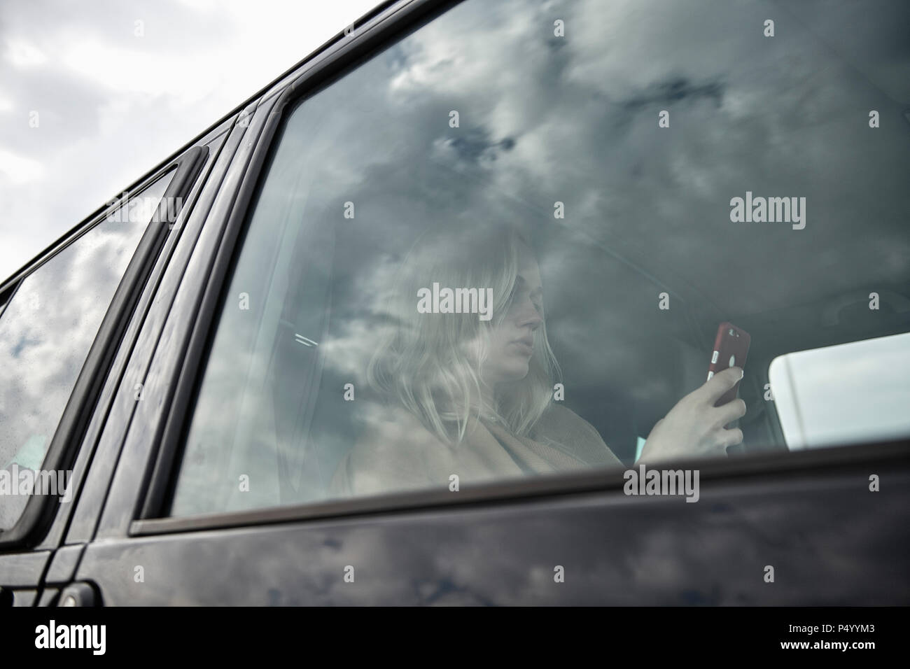 Jeune femme assise dans une voiture à la recherche de téléphone cellulaire Banque D'Images