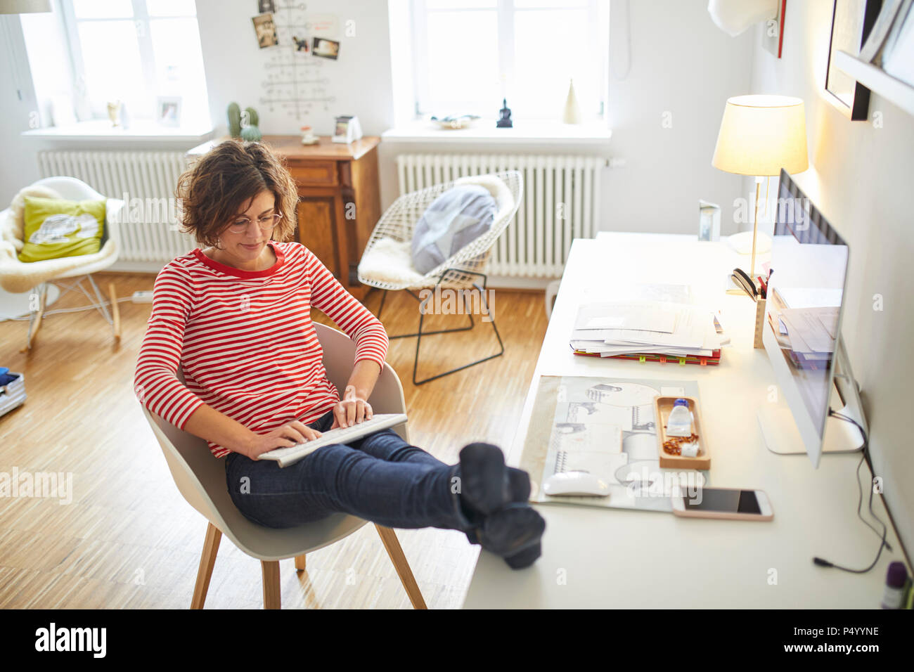 Young woman avec les pieds jusqu'au bureau à domicile à l'aide de clavier sans fil Banque D'Images