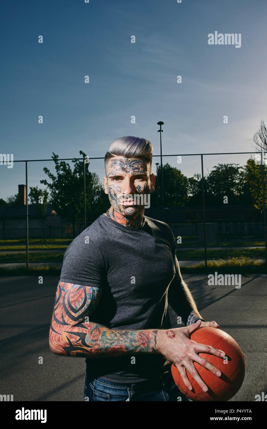 Portrait de jeune homme tatoué avec le basket-ball sur cour Banque D'Images