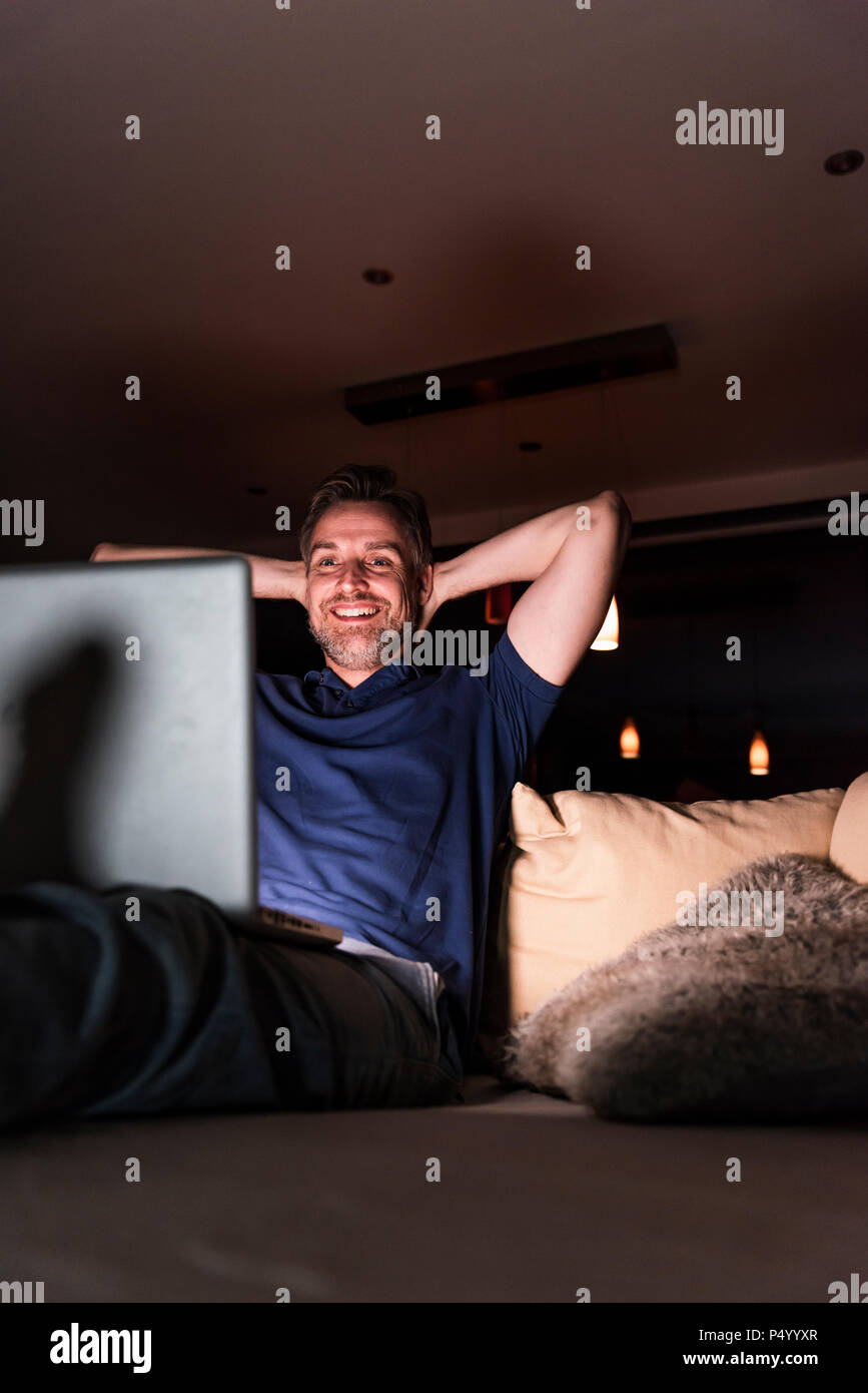 Man sitting on sofa at home looking at laptop Banque D'Images