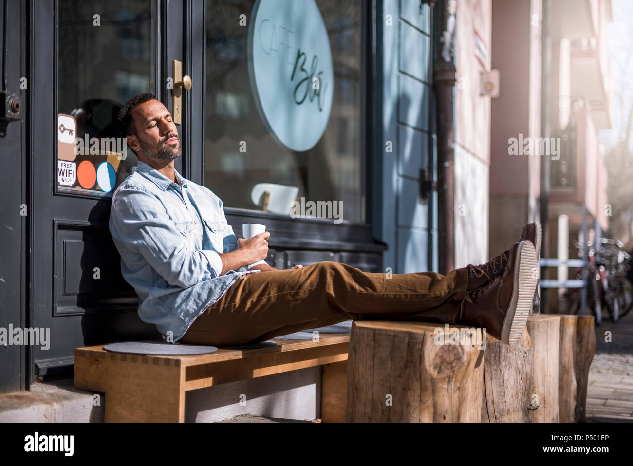 Homme assis détendue d'un café à l'extérieur le soleil brille, Banque D'Images