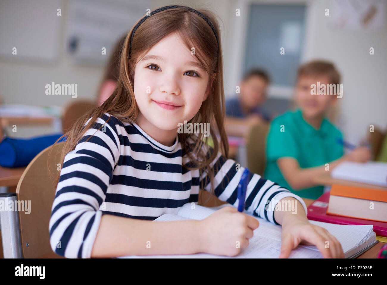 Portrait of smiling schoolgirl écrit dans un livre d'exercices en classe Banque D'Images
