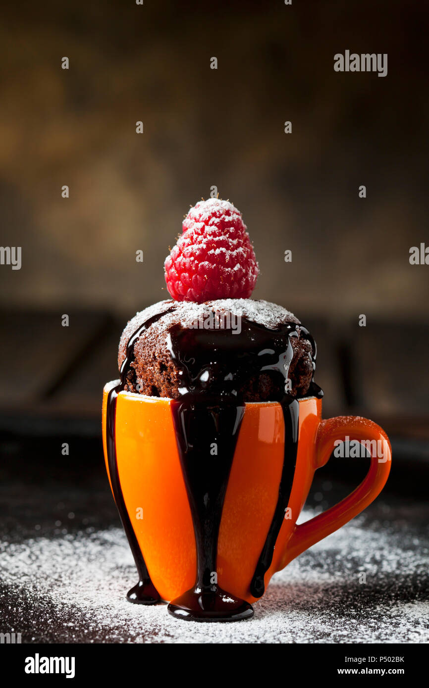 Cup cake au chocolat avec sucre glace, sauce chocolat et framboise Banque D'Images