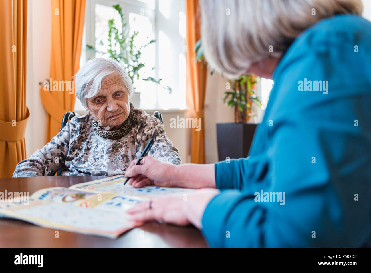 Femme prendre soin de vieille femme doing crossword puzzle Banque D'Images