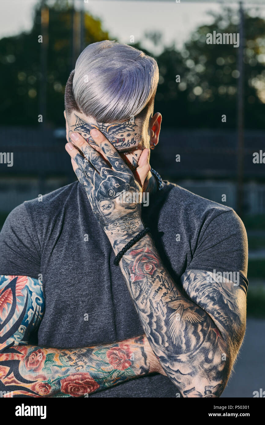 Jeune homme tatoué à l'extérieur se cacher son visage Banque D'Images