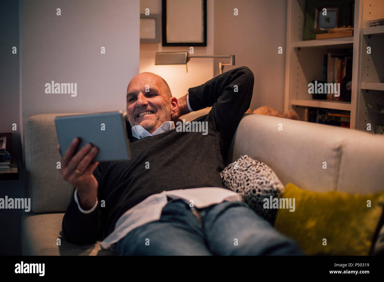 Man lying on couch, lecture d'e-book Banque D'Images