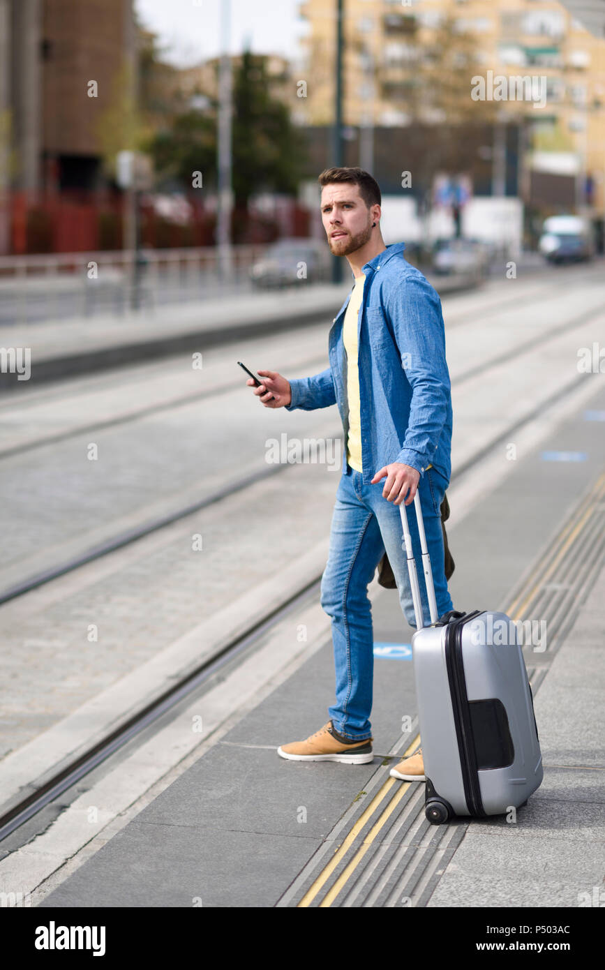 Jeune homme l'attente à une station avec le smartphone à la main et chariot Banque D'Images