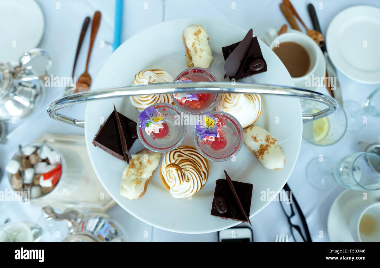 Regardant vers le bas sur une table avec un thé anglais l'après-midi, une plaque ronde de gâteaux colorés à l'argent d'un plateau/bouilloire et tasses pots blanc blanc li Banque D'Images