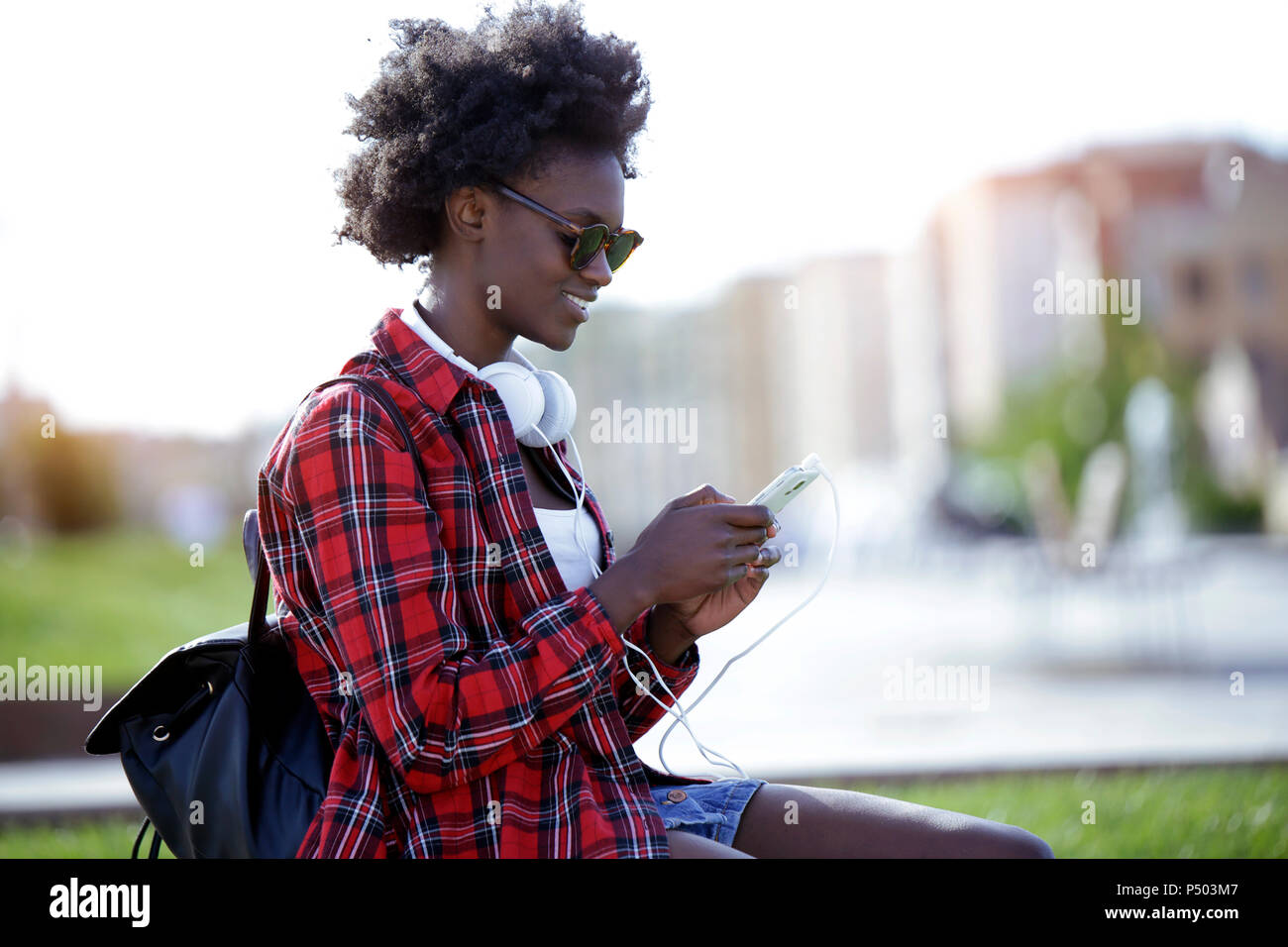 Souriante jeune femme avec sac à dos et casque using cell phone Banque D'Images