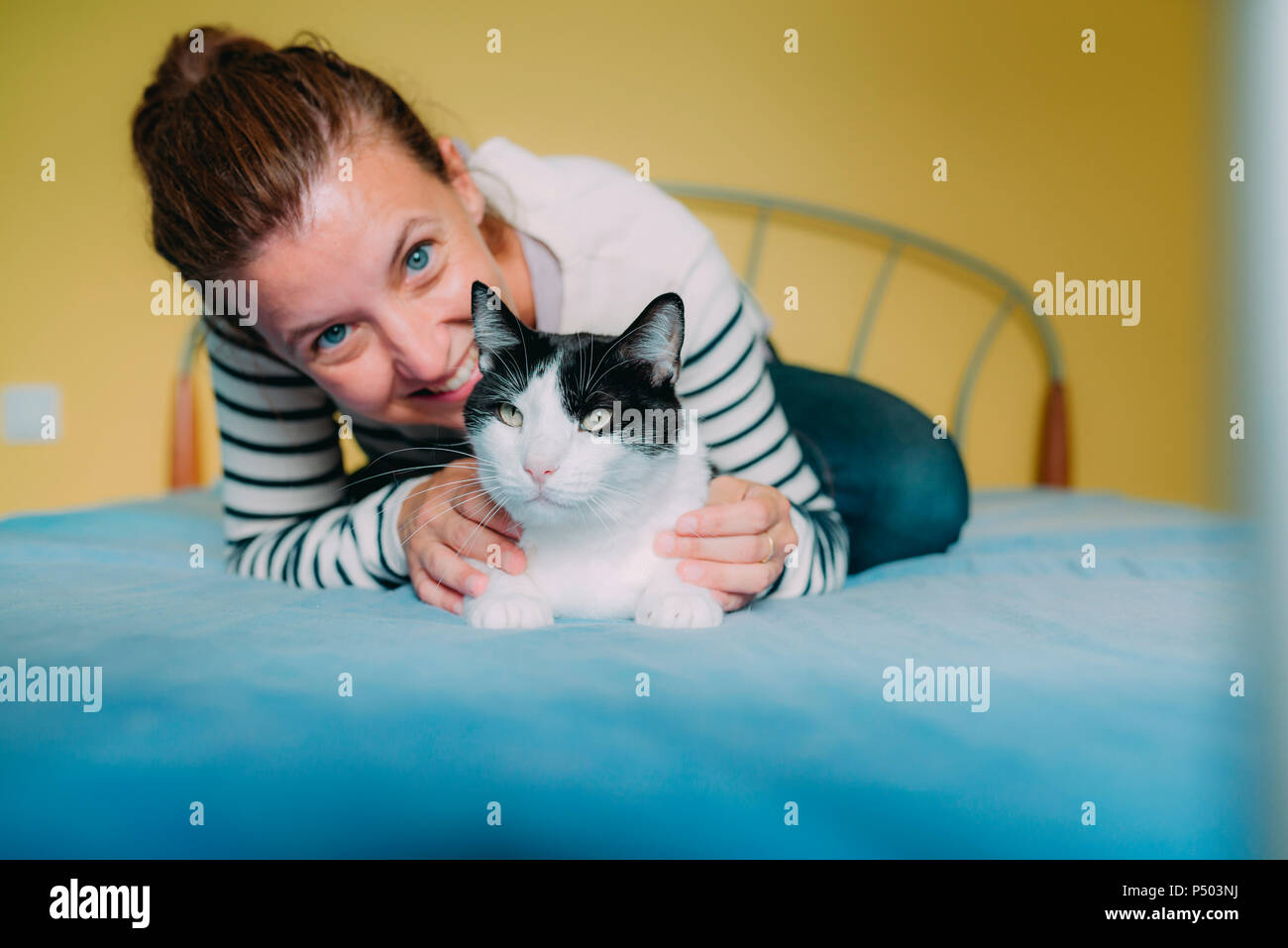 Femme heureuse avec un chat noir et blanc sur le lit Banque D'Images