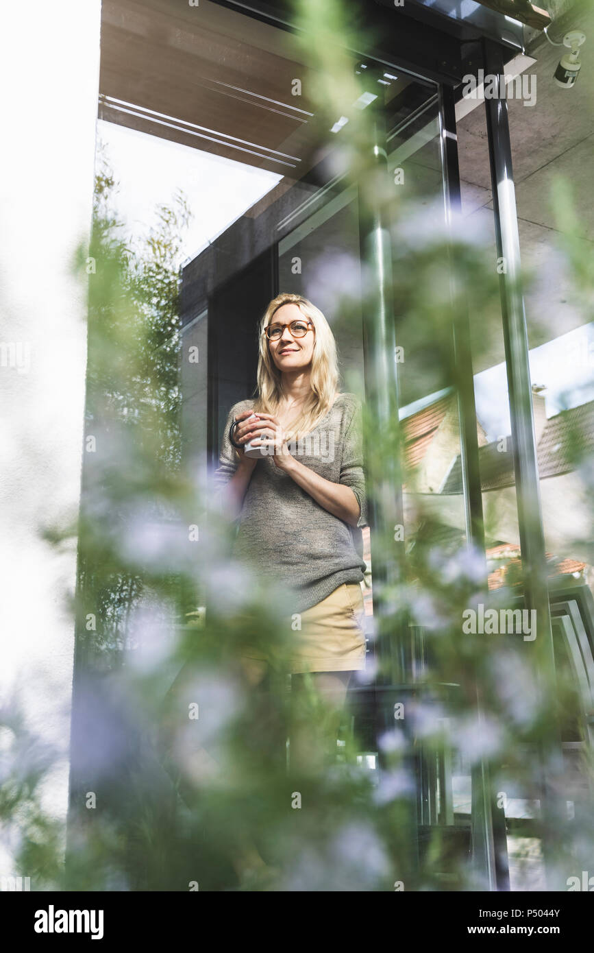 Contenu mature woman with coffee mug debout devant sa maison Banque D'Images