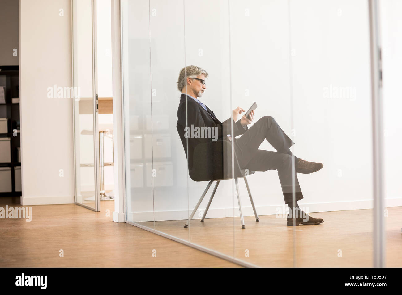 Businessman sitting on chair, using digital tablet Banque D'Images
