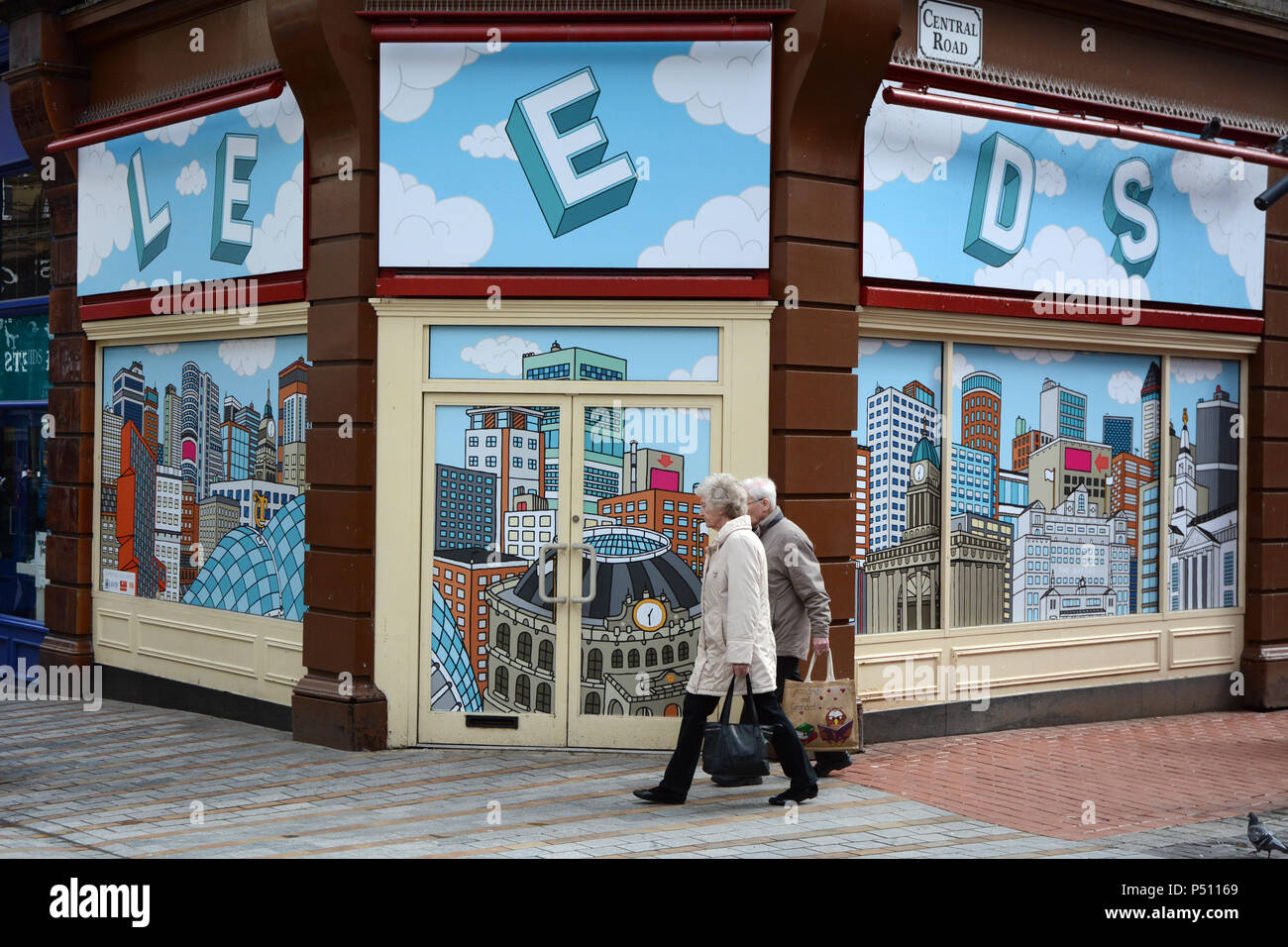 Un couple de personnes âgées passent devant une vitrine vide avec un fond d'illustration de la ville de Leeds, Leeds en Angleterre, Royaume-Uni. Banque D'Images