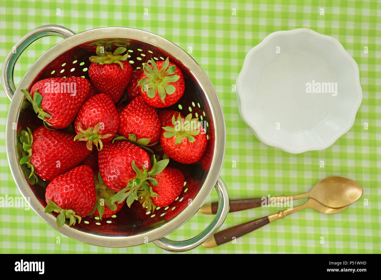 Les fraises de saison frais dans une passoire avec des bols et des cuillères de frais généraux. L'horizontale et tourné en lumière naturelle. Banque D'Images