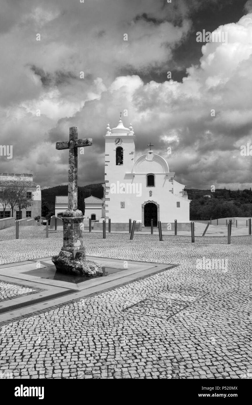 Image en noir et blanc de la croix et de l'église dans la place principale de Querenca, Portugal Banque D'Images