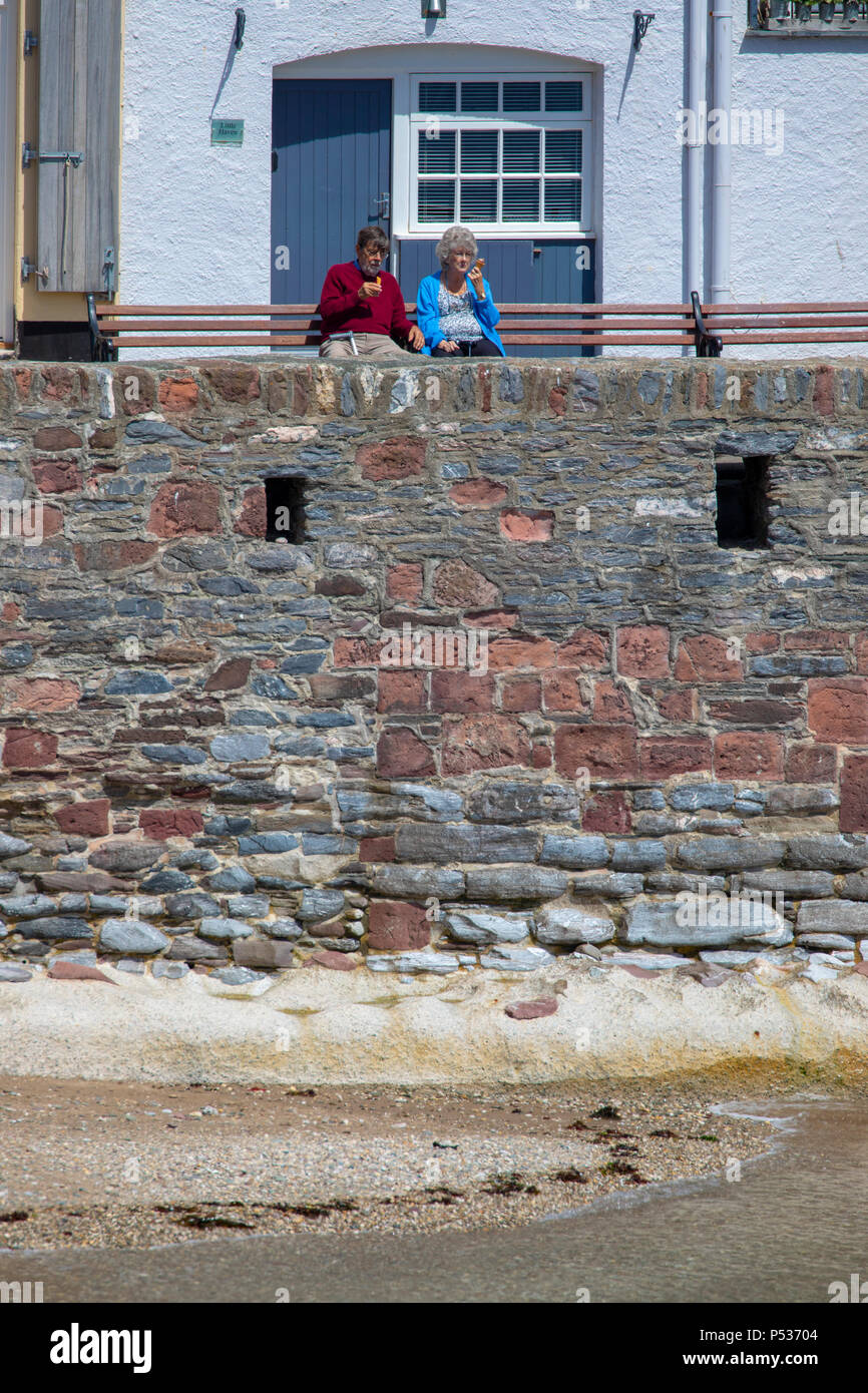 Un couple bénéficiant d'une glace assis sur un banc du port pittoresque et le pittoresque village de pêcheurs de Cawsand à Cornwall, England, UK Banque D'Images