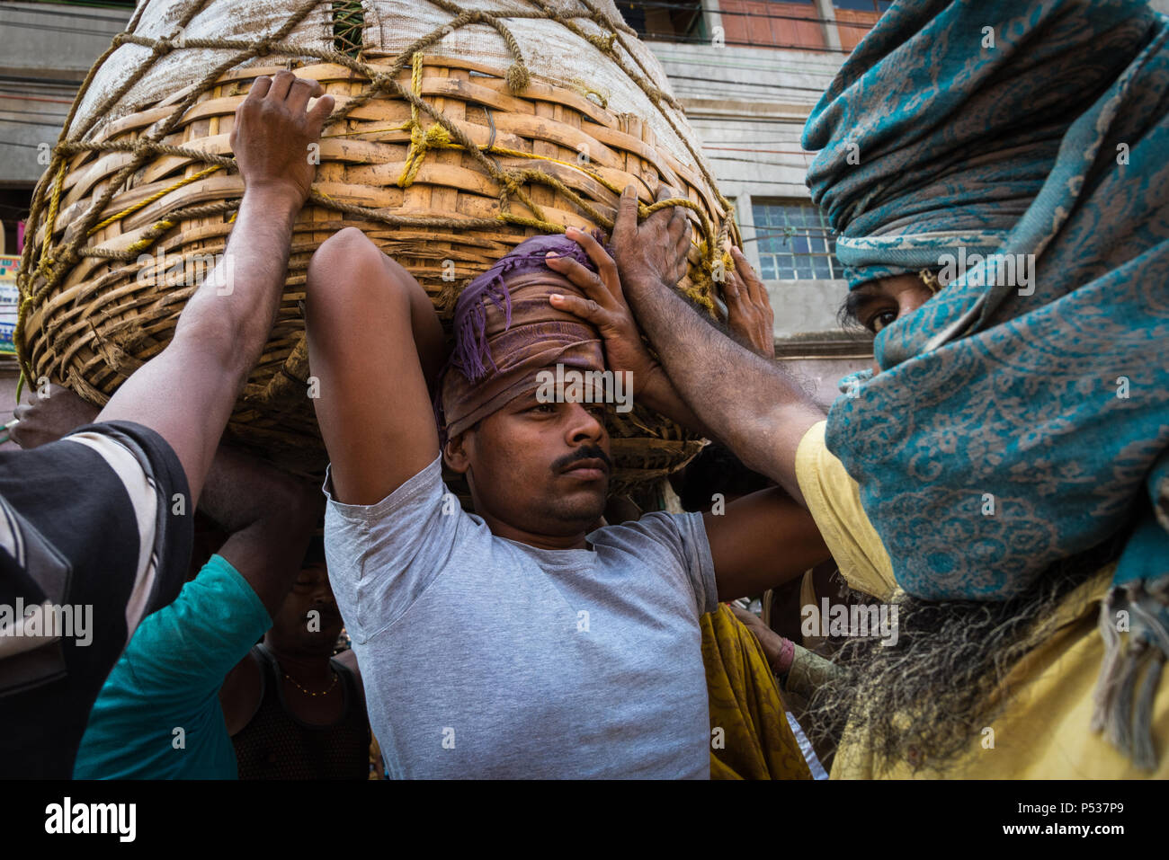 Les hommes de ramasser une lourde charge de marchandises en Koley Marché, Kolkata, Inde. Banque D'Images