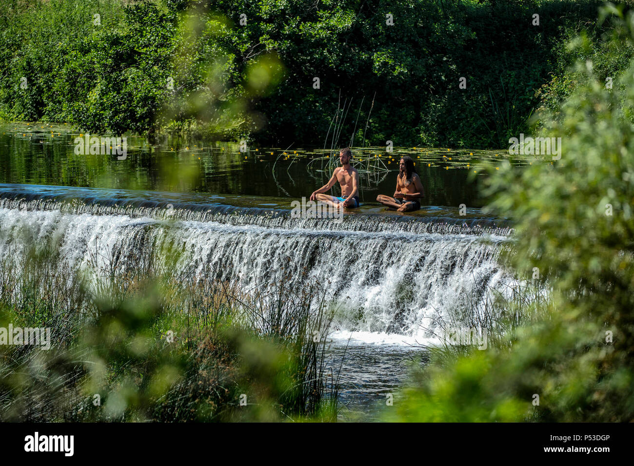 Deux hommes méditer dans l'eau à Warleigh Weir sur la rivière Avon près de Bath dans le Somerset sur une chaude journée d'été. Banque D'Images