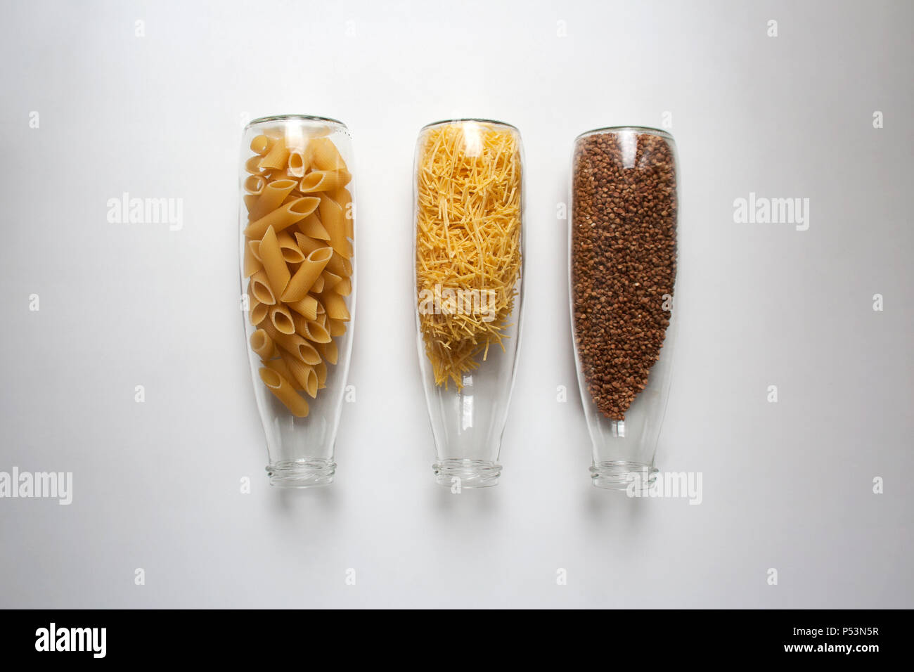 Penne Rigate, pâtes aux œufs et le sarrasin dans des contenants en verre transparent isolé sur fond blanc d'un high angle view Banque D'Images