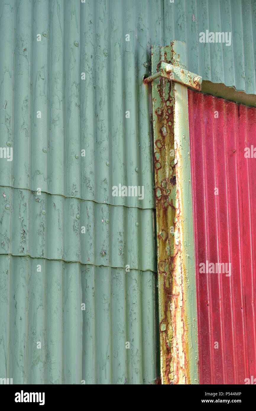 Le vert pâle et rouge mur extérieur fabriqués à partir de tôle ondulée avec quelques taches de rouille. Banque D'Images