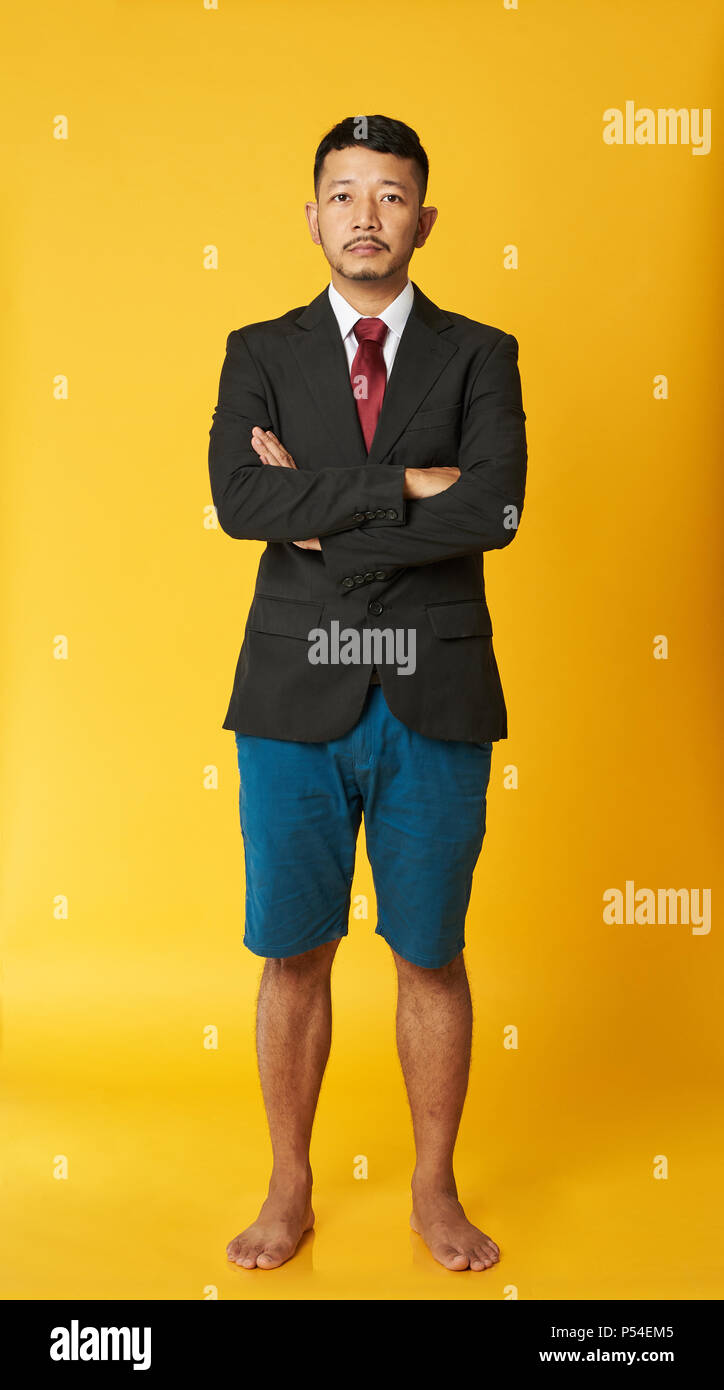 L'homme d'affaires asiatiques en short et bras croisés isolé sur fond jaune Banque D'Images