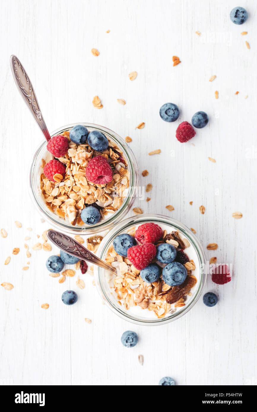 Deux pots de yogourt et petits fruits, granola sur table en bois blanc. Vue d'en haut. Banque D'Images