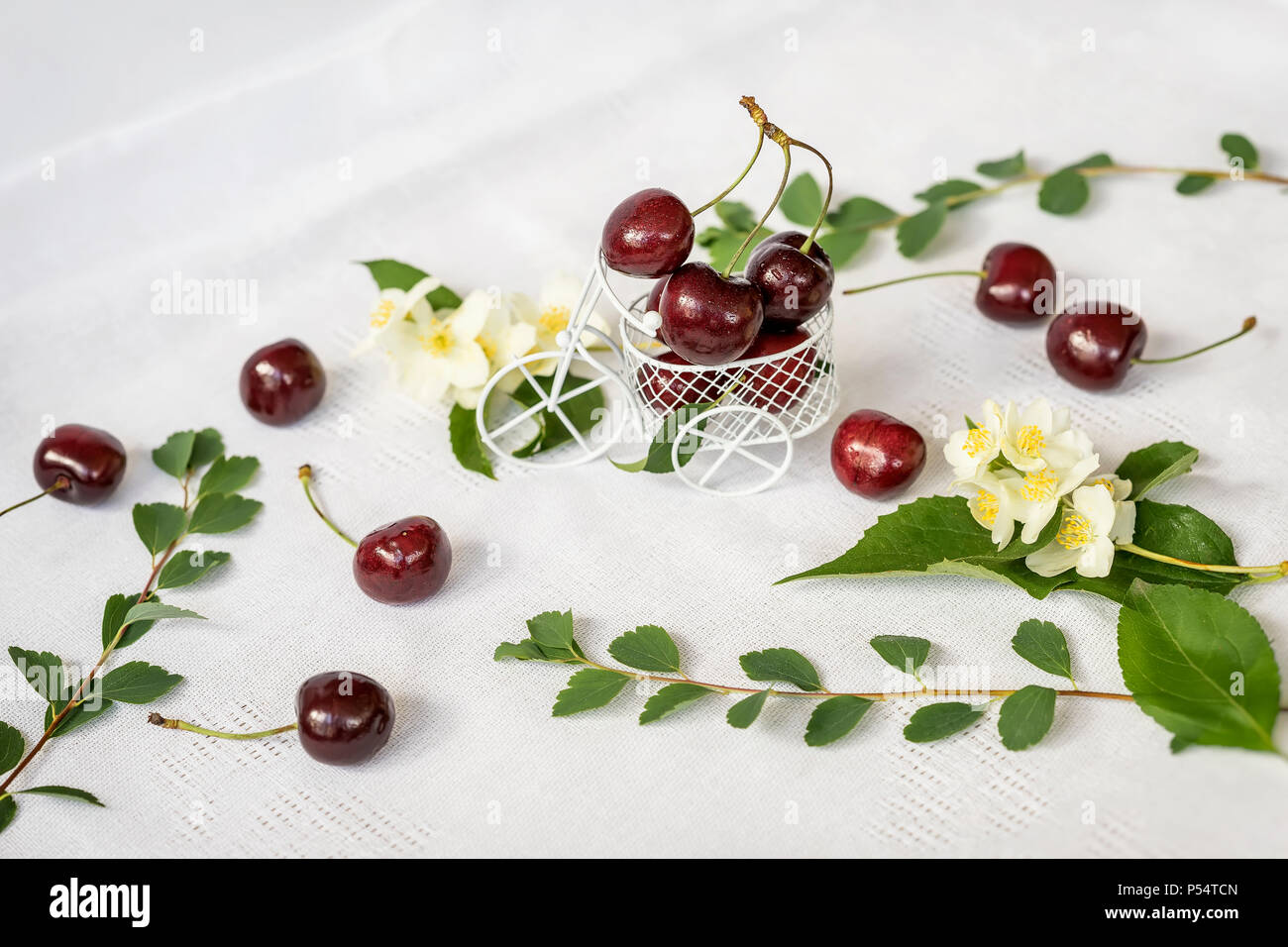 Jouet miniature panier, chariot avec cerise mûre, fleurs de jasmin, feuillage vert sur fond clair. Concept d'une alimentation saine, de désintoxication, les vitamines, les régimes Banque D'Images