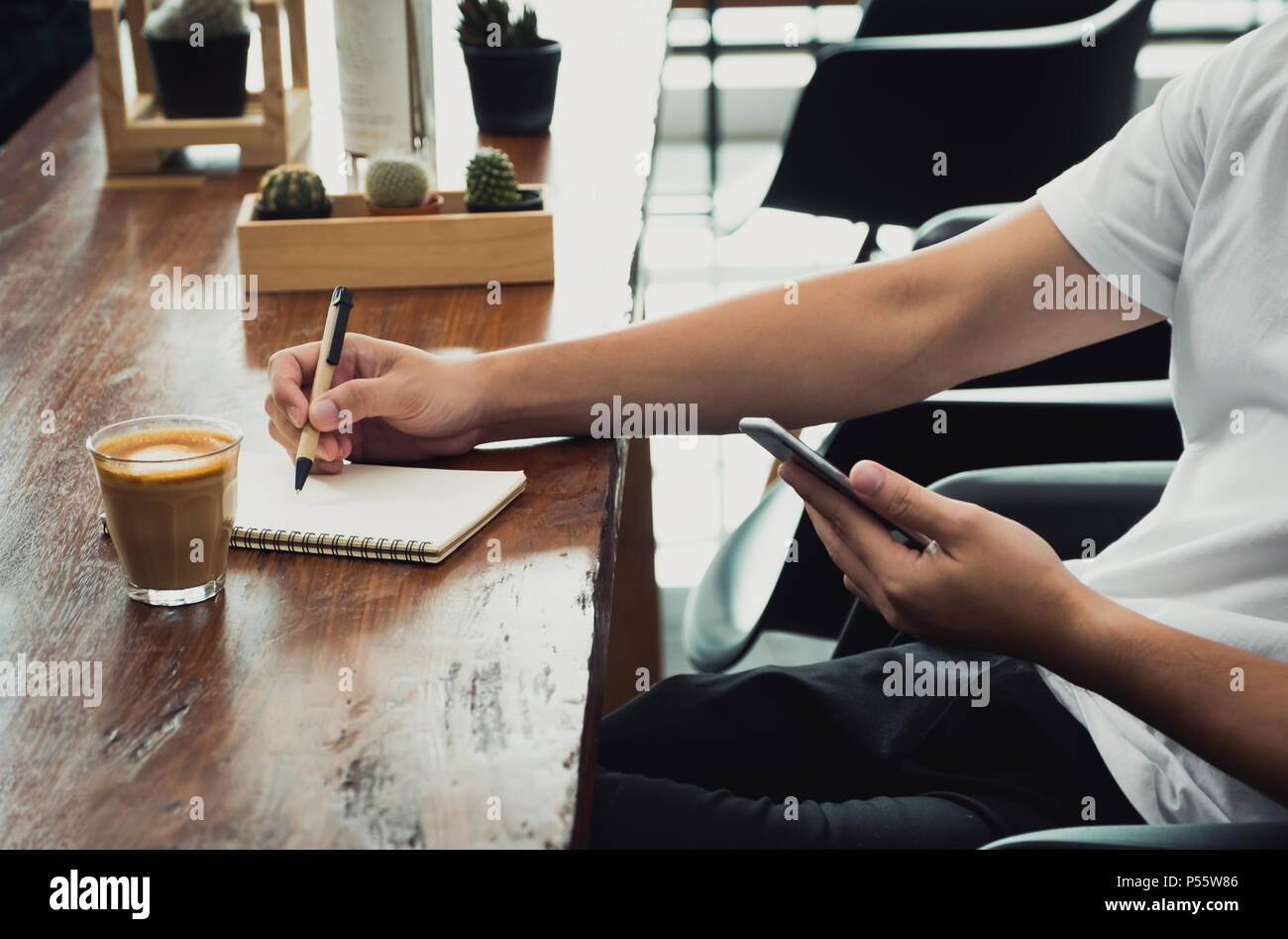 Gros plan homme asiatique occasionnel utiliser téléphone mobile et de l'écriture sur ordinateur portable sur la table en bois dans la région de coffee shop en ligne moderne,de vie numérique de travail concept.influe Banque D'Images