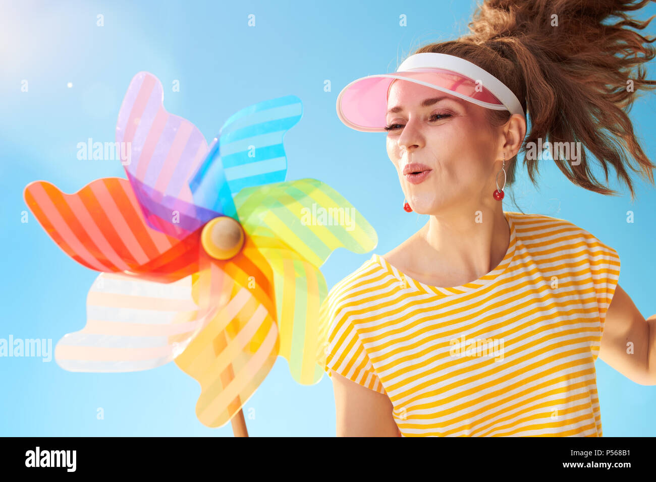 Happy fit femme en chemise jaune sur fond de ciel bleu en soufflant sur moulin colorés Banque D'Images