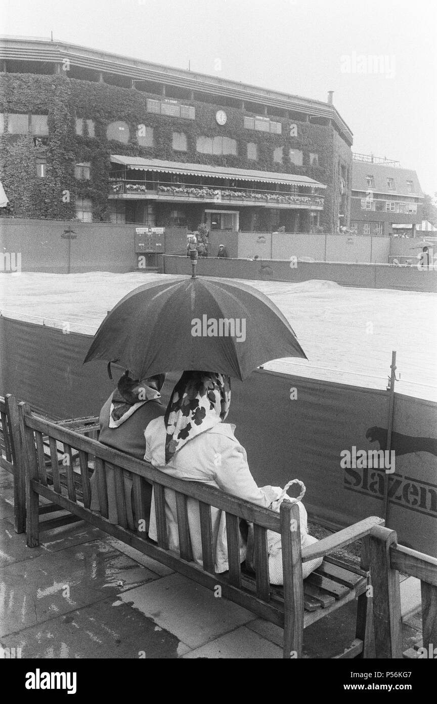 Le temps humide s'arrête de jouer à Wimbledon. Fans fidèles s'asseoir que le mauvais temps avec leur parapluie, partagé avec le Centre Court dans l'arrière-plan. Photo prise le 24 juin 1983 Banque D'Images