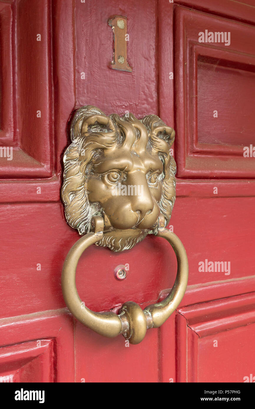 Ancienne tête de lion en métal en laiton heurtoir sur panneaux de bois peints en rouge chambre porte avant, England, UK Banque D'Images