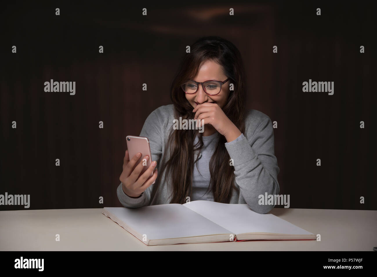 Young woman using mobile phone while reading book Banque D'Images