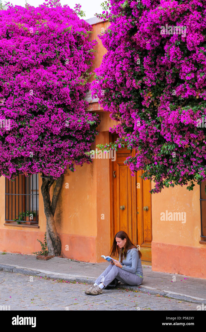 Young woman reading book sur un trottoir dans quartier historique de Colonia del Sacramento, Uruguay. C'est l'une des plus anciennes villes de Uruguay Banque D'Images