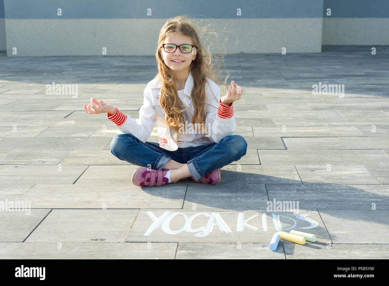 Petite fille en position du lotus, la pratique du yoga. Sur l'asphalte, les enfants yoga texte écrit par l'enfant crayons de couleur Banque D'Images