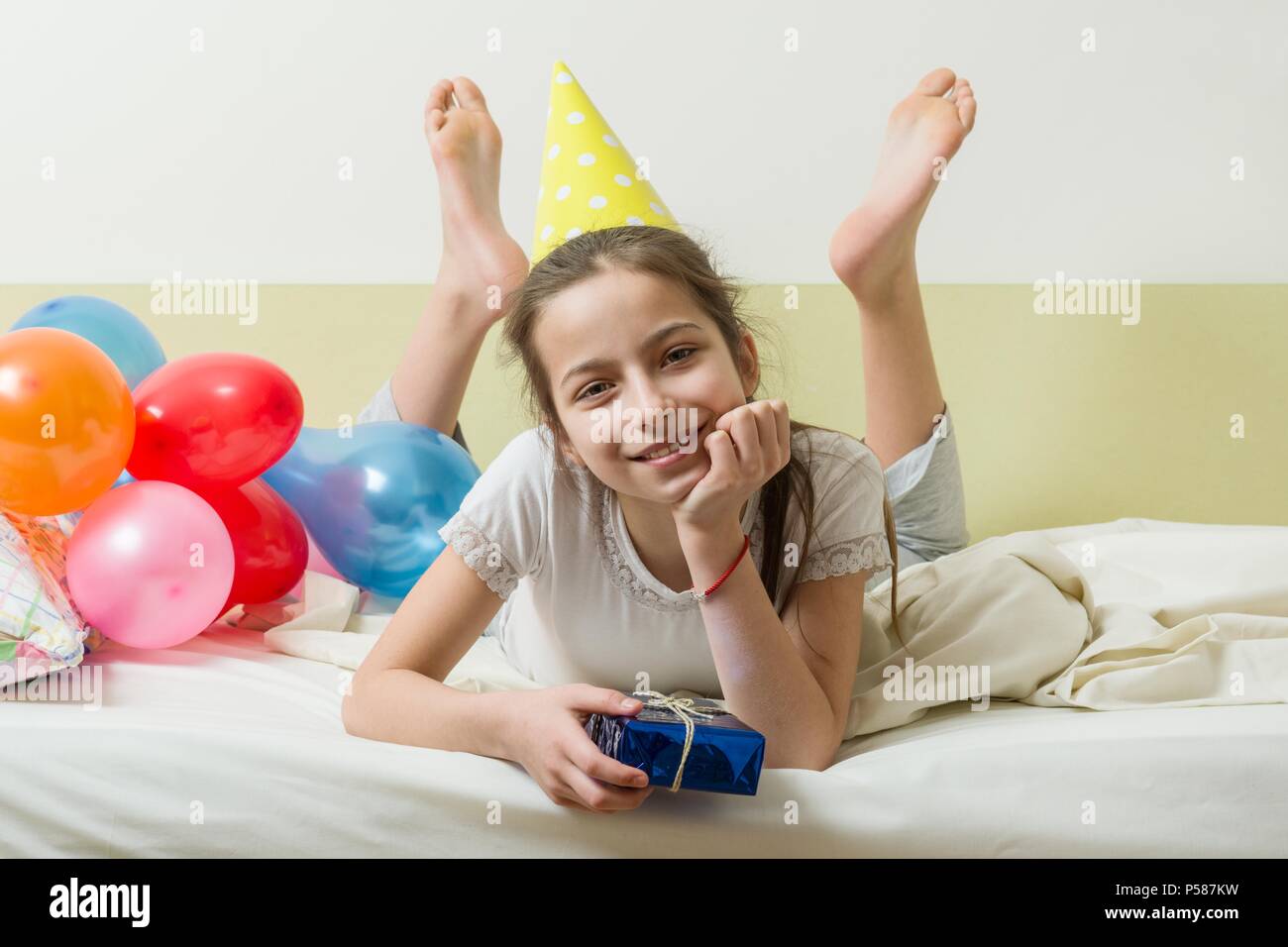 L Anniversaire D Une Adolescente Est De 10 11 Ans Une Fille Dans Un Chapeau De Fete Avec Un Cadeau Se Trouve Sur Le Lit Dans Une Chambre D Enfants Des Ballons D Arriere Plan Photo Stock L Anniversaire D Une Adolescente Est De 10 11 Ans Une Fille Dans Un Chapeau De Fete Avec Un Cadeau Se Trouve Sur Le Lit Dans Une Chambre D Enfants Des Ballons D Arriere Plan Photo Stock