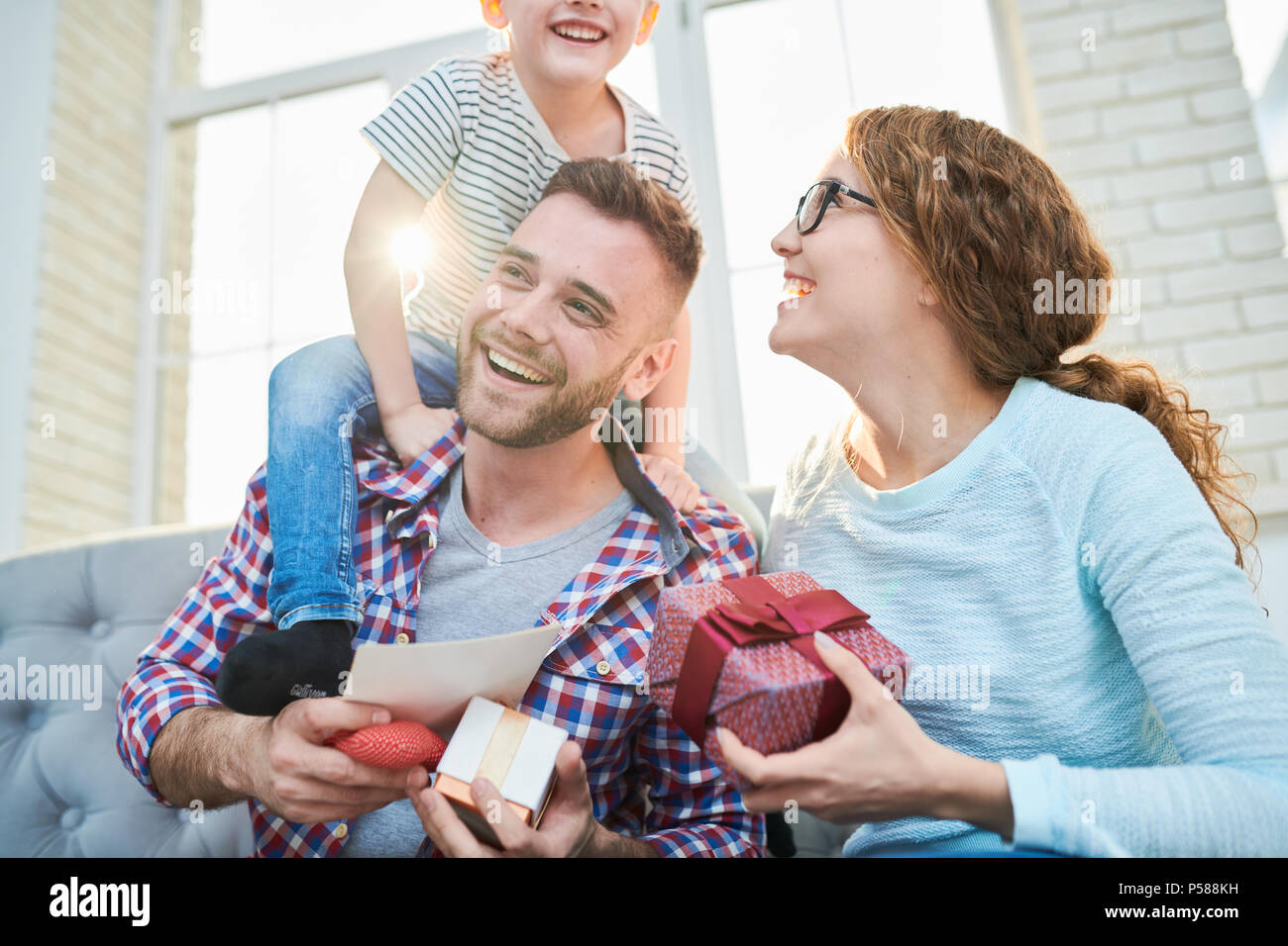 Portrait de tons chauds, le holding de la famille heureux ludique présente l'implantation sur le canapé dans la salle de séjour à la maison, l'accent sur smiling handsome man Banque D'Images