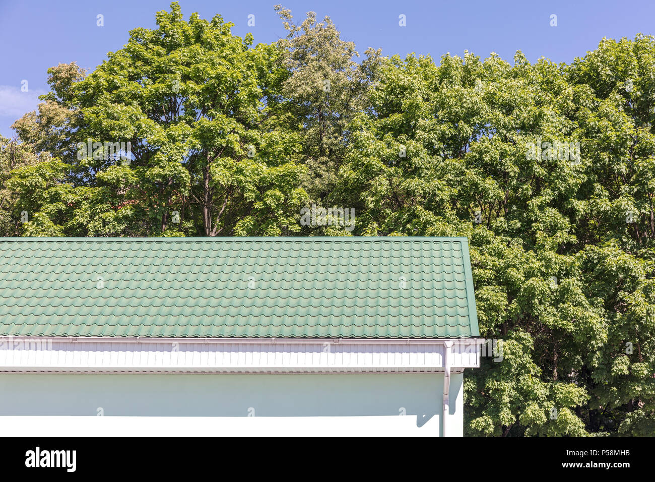 Toit en métal vert et blanc gouttière système. nouvelle maison contre des arbres verts dans la lumière du soleil Banque D'Images