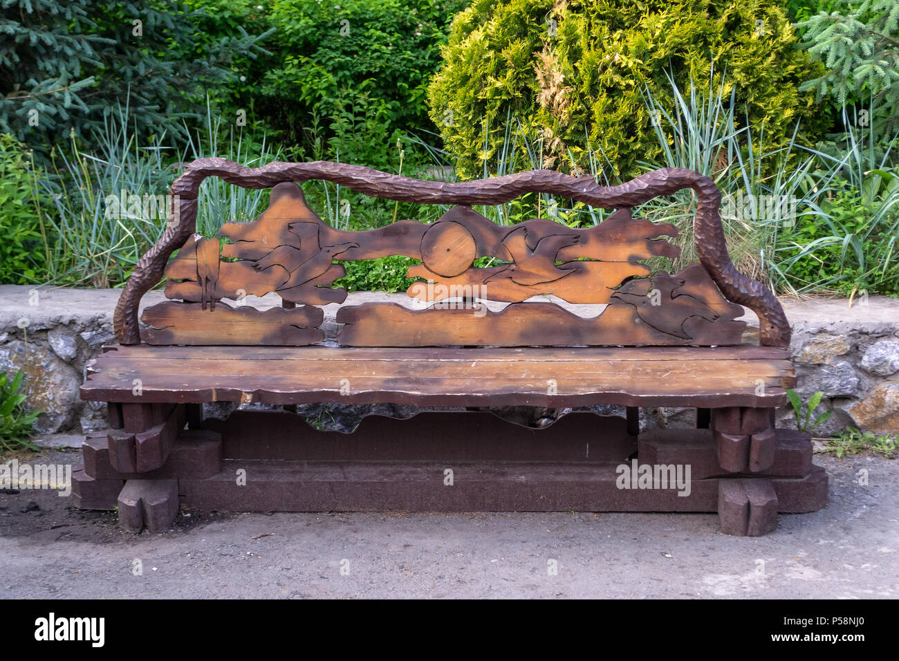 Un banc en bois fait à la main avec du bois et panneaux peints avec de la peinture marron avec un modèle sculpté d'animaux et d'oiseaux sur le dos contre le ba Banque D'Images