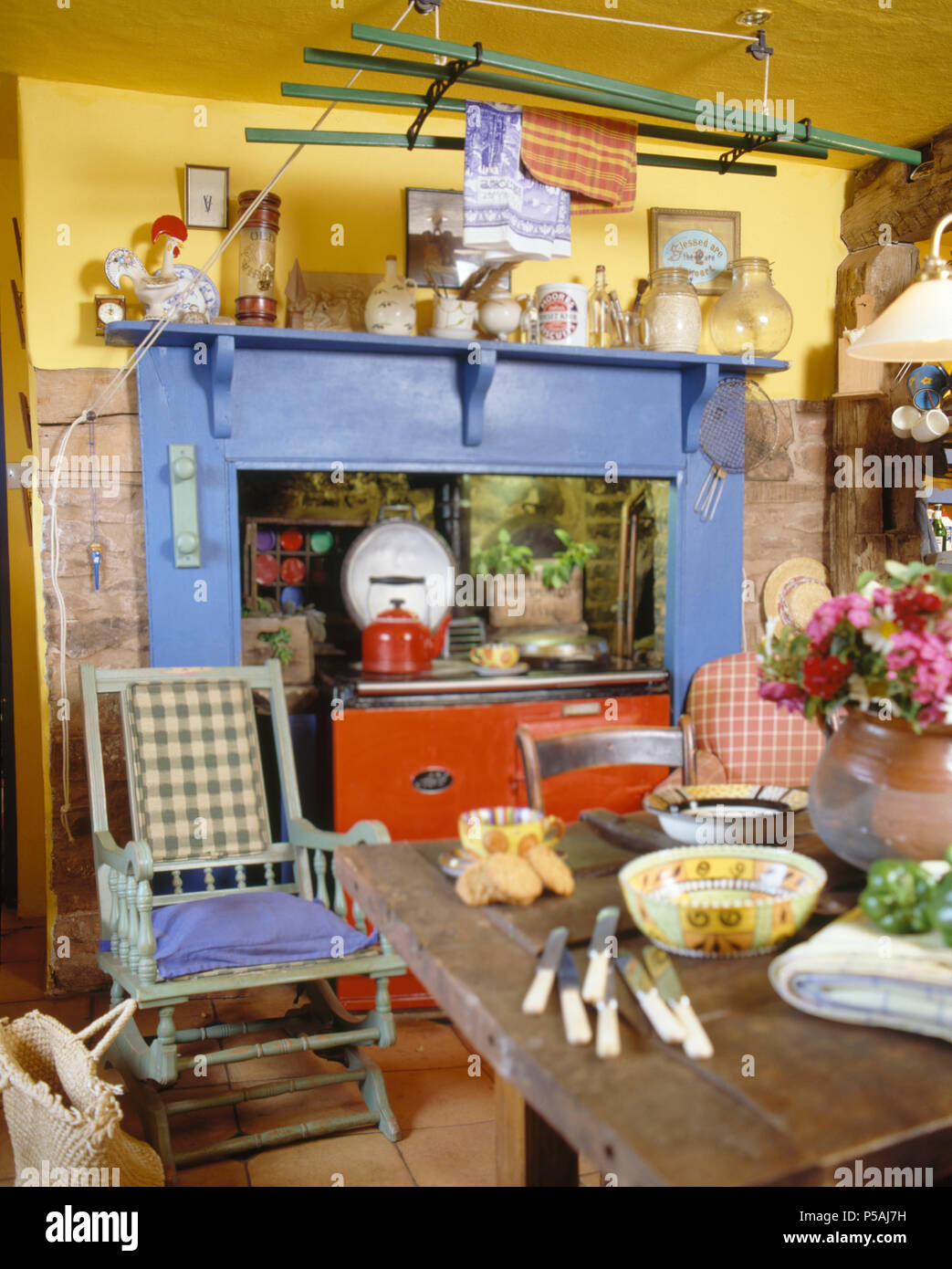 Rocking chair peint en face de Aga orange avec cheminée peinte en bleu en cuisine de campagne Banque D'Images