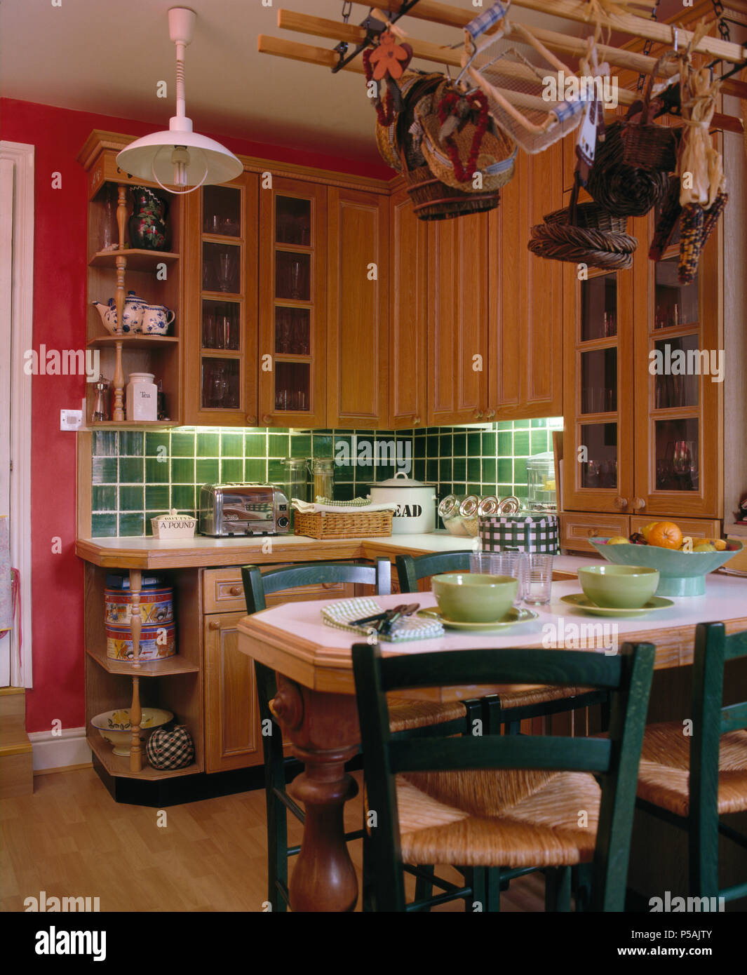 Rush vert chaises assis à table pour le déjeuner dans la cuisine de campagne rose avec carrelage vert au-dessus du plan de travail Banque D'Images