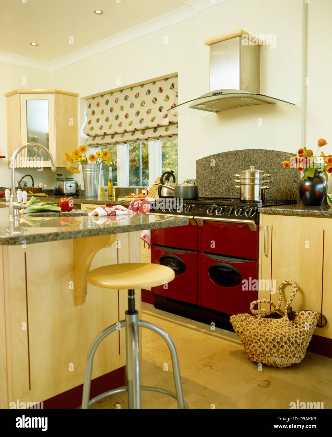 Tabouret en bois clair +chrome au petit déjeuner bar dans une cuisine moderne avec cuisinière four rouge Banque D'Images