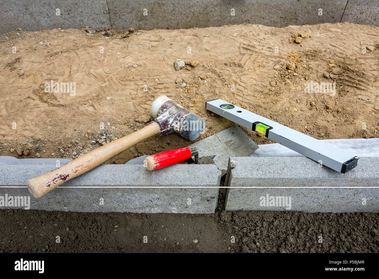 La définition retenue de pointe acheter mettant un frein aux frontières des pierres à terre-humide avec béton maillet en caoutchouc, truelle et niveau à bulle Banque D'Images