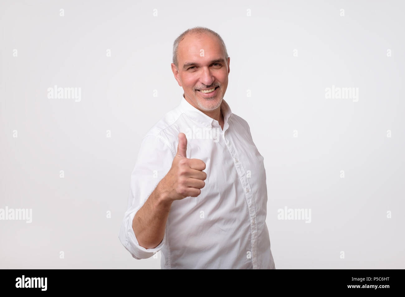 Handsome man en chemise blanche montre pouce vers le haut. Il est satisfait de sa condition financière et la santé Banque D'Images